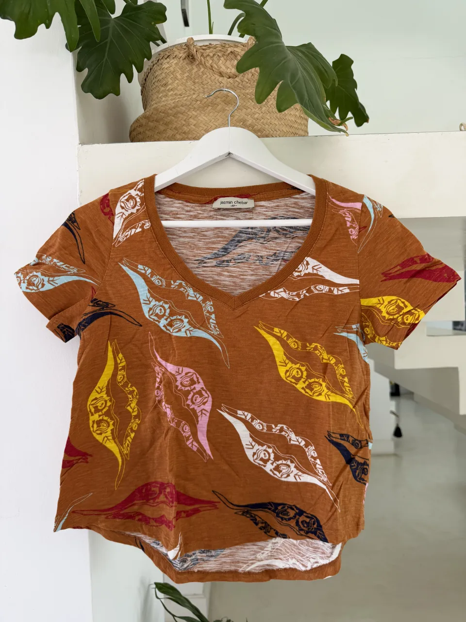 Remera de manga corta con cuello en V y estampa de hojas en tonos tierra, rosa, amarillo y azul.