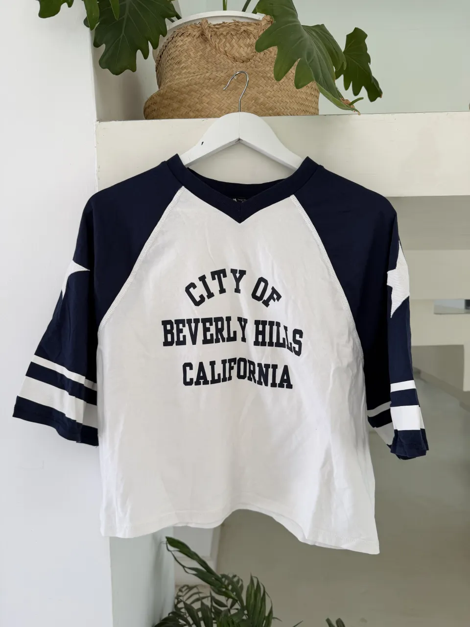 Remera manga corta raglán blanca con mangas y cuello azul marino. Estampado frontal "CITY OF BEVERLY HILLS CALIFORNIA" en azul. Rayas horizontales en los puños de las mangas.