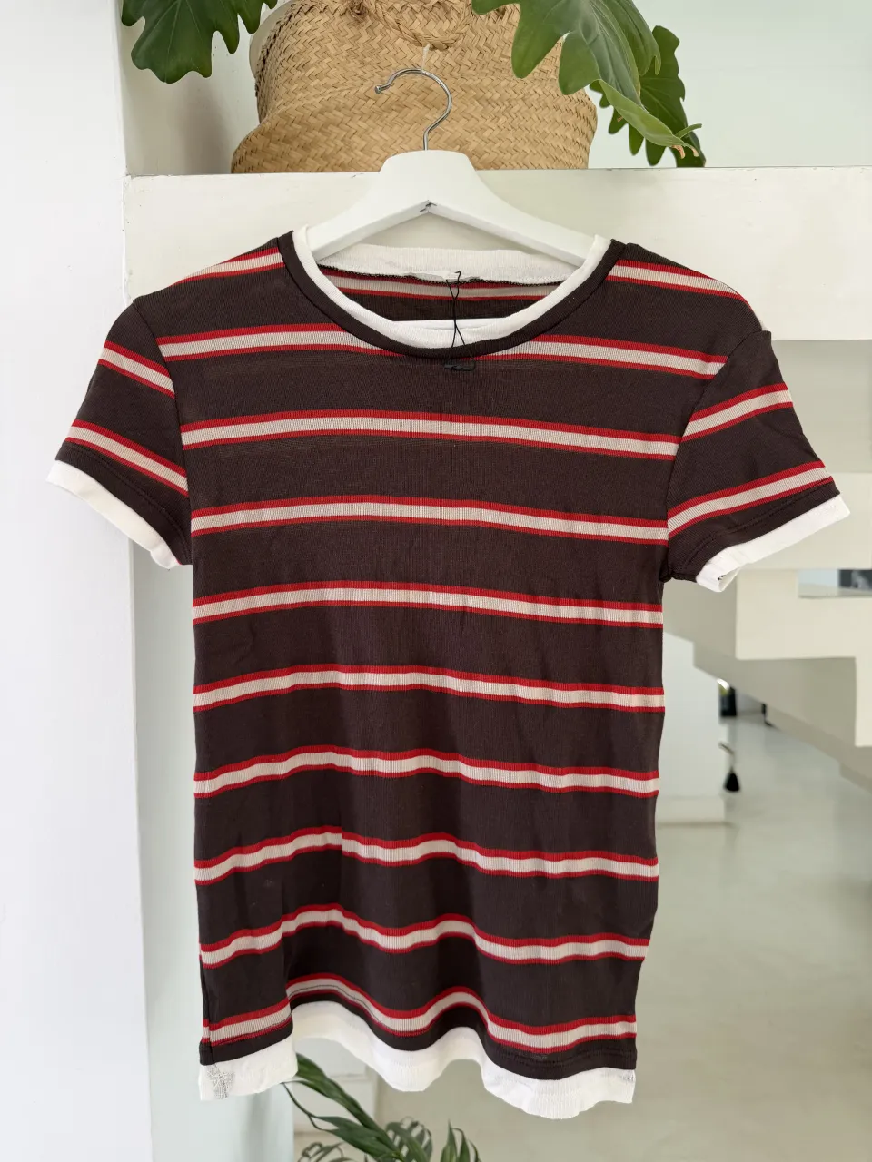 Remera a rayas marrones, rojas y blancas con cuello redondo y mangas cortas. Los bordes de las mangas y el cuello son blancos.