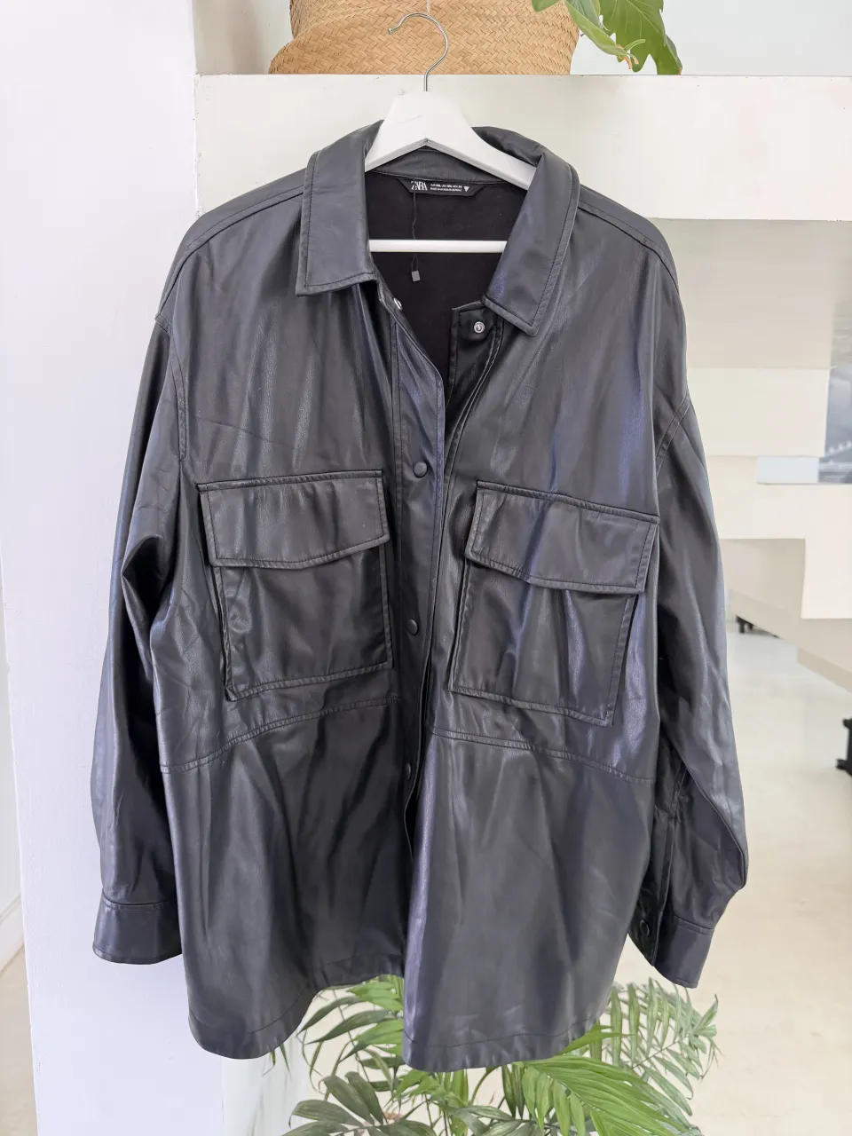 Campera de cuero sintético negra con dos bolsillos frontales con tapa y botones. Le falta en una manga un botón.