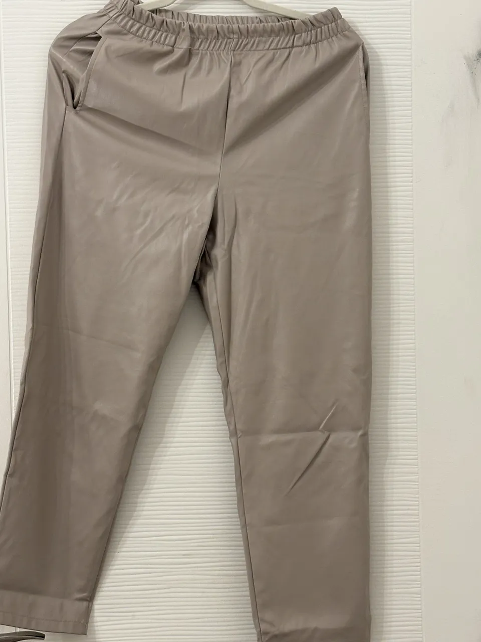 Pantalón de cuero sintético color tiza, tiro alto con cintura elastizada y bolsillos. Un básico moderno y canchero para looks de día o noche.