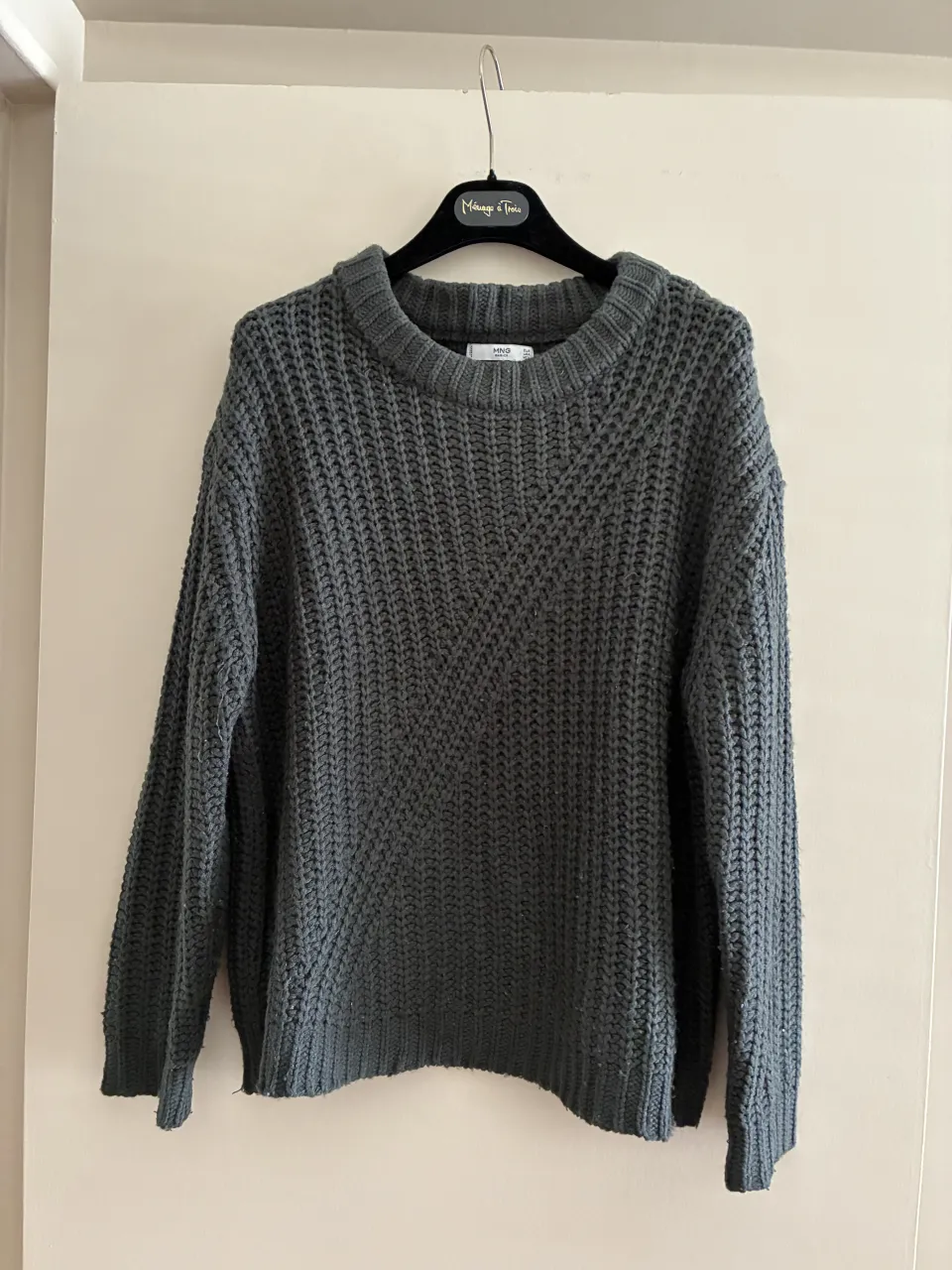 Sweater de tejido grueso con cuello redondo y mangas largas. Presenta un diseño de tejido cruzado en la parte delantera.