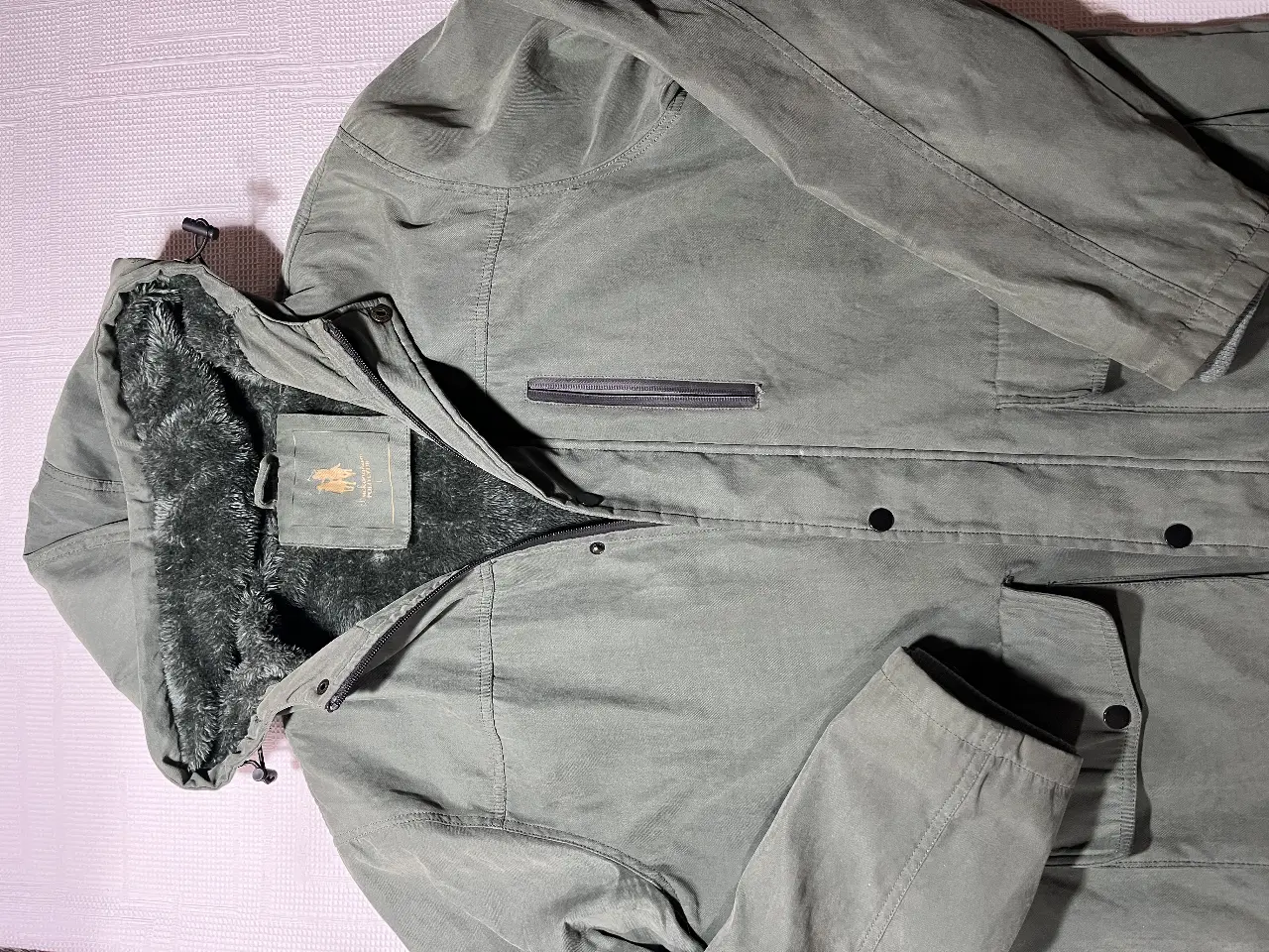 Campera de abrigo para hombre, color verde militar, con capucha y forro de piel sintética. Posee cierre y bolsillos. Ideal para el invierno.