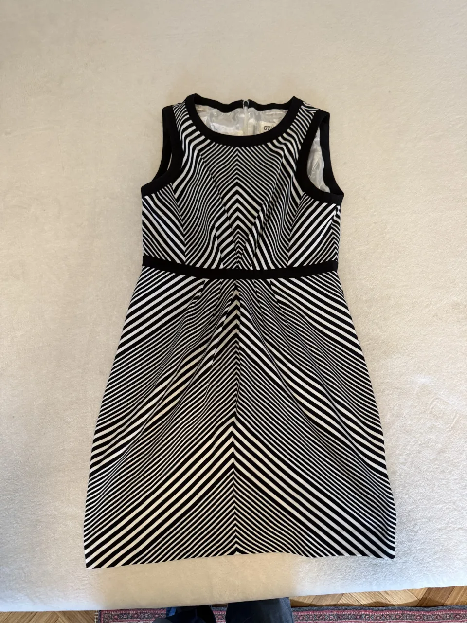 Vestido corto sin mangas, con cuello redondo y cierre en la espalda. Estampado a rayas diagonales en blanco y negro.