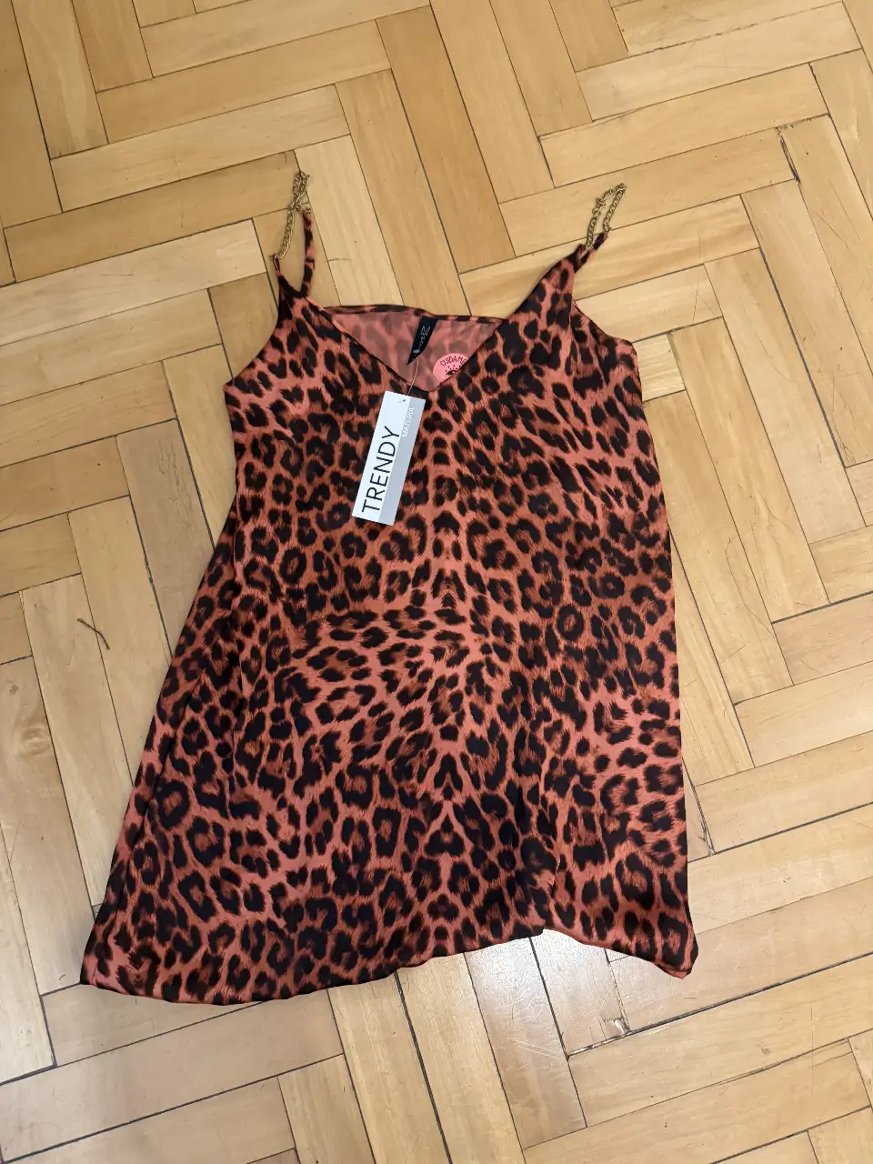 Vestido mini con estampado de leopardo en tonos naranja y marrón. Con tirantes dorados y etiqueta 'Trendy'. Ideal para una salida o fiesta.