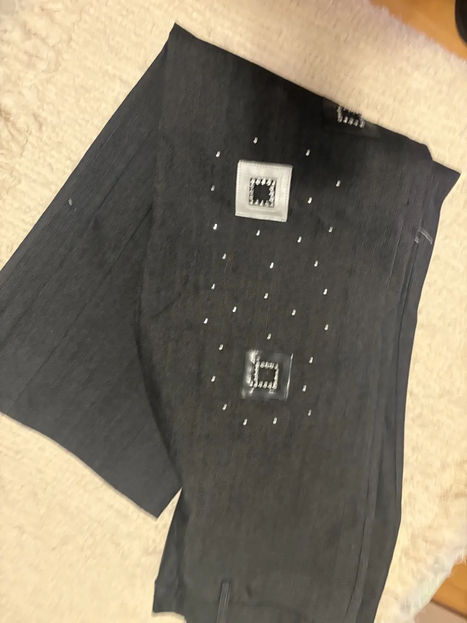 Pantalón de jean oscuro con apliques cuadrados plateados y detalles de strass.