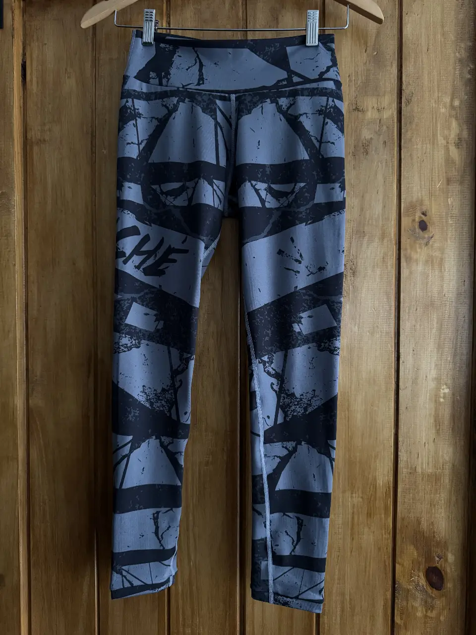 Calzas deportivas grises con estampado geométrico en negro. Ideales para entrenar o para un look casual y cómodo.