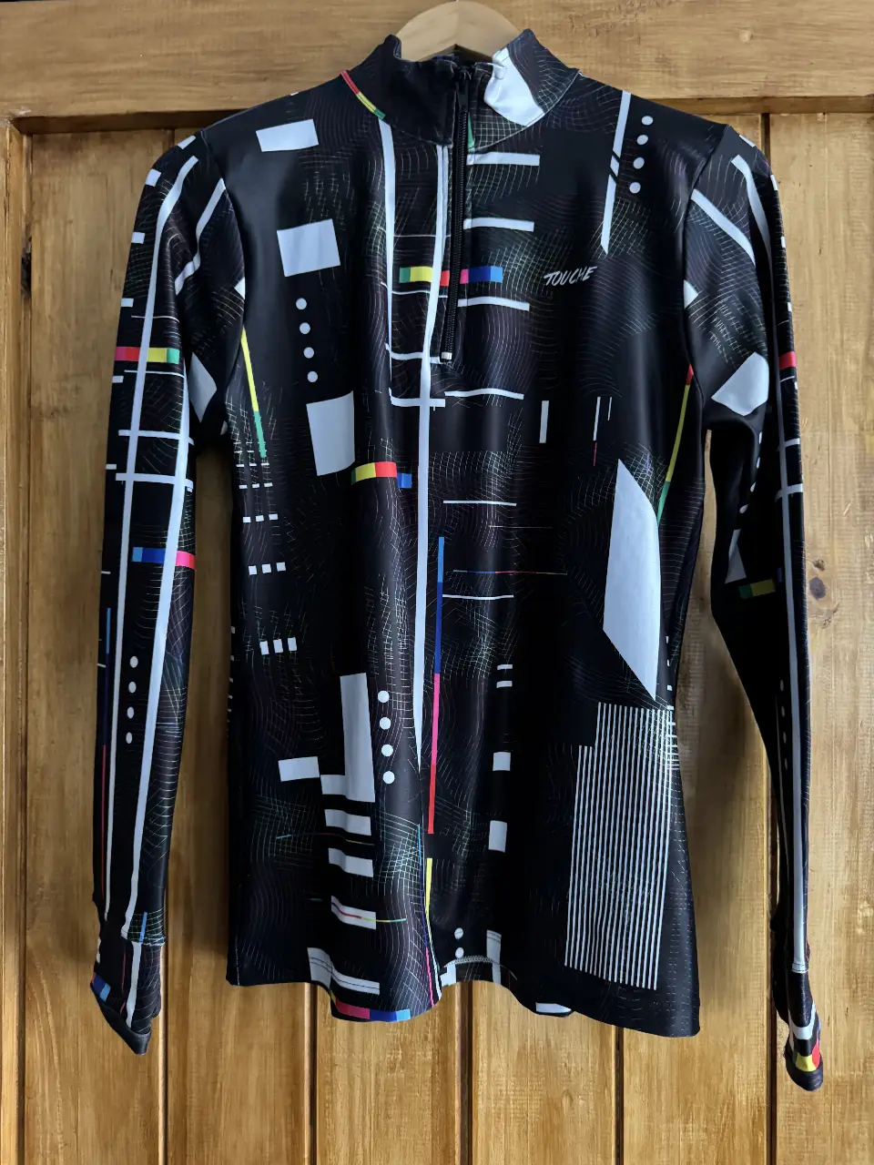 Remera deportiva de manga larga con diseño geométrico en blanco y negro. Cuello alto con cierre. Ideal para running y actividades al aire libre.