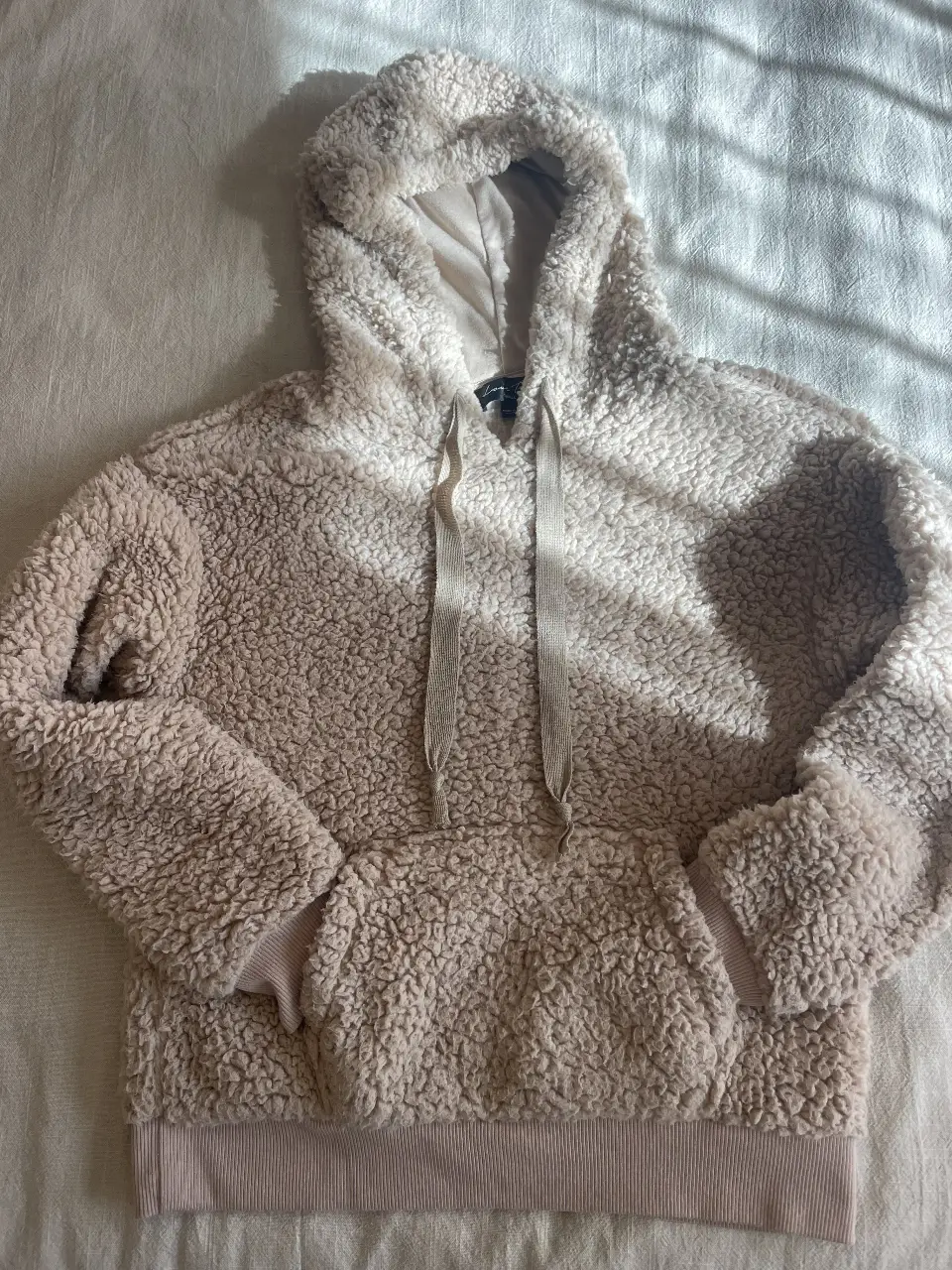 Buzo canguro talle small de tela tipo sherpa, suave y abrigado, ideal para el invierno. Posee capucha con cordones y bolsillo frontal. Perfecto para un look casual y cómodo.