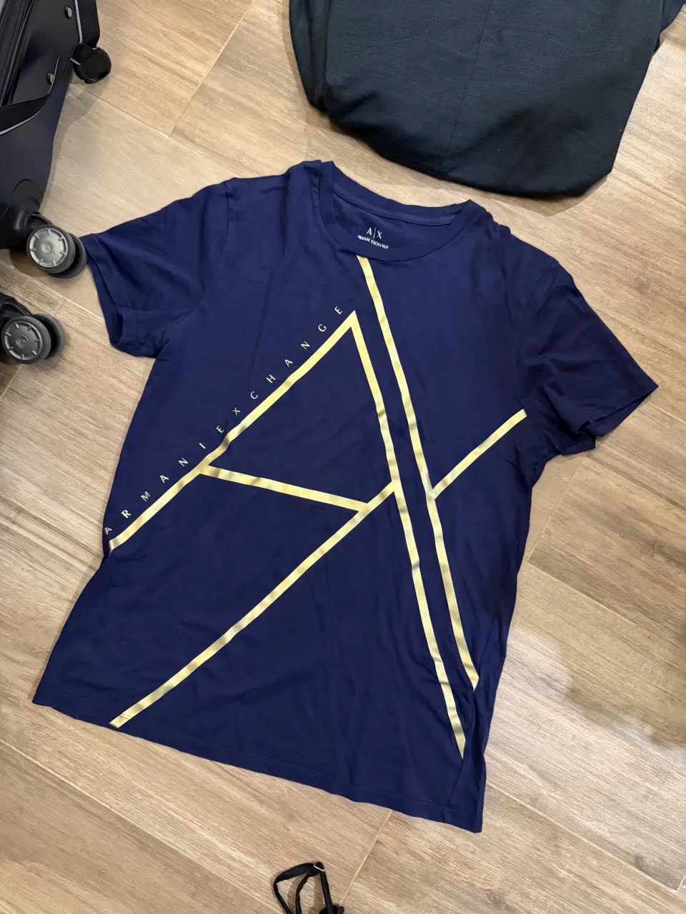 Remera azul marino con estampa geométrica en color dorado. La estampa incluye el logo de la marca y el texto "ARMANI EXCHANGE".