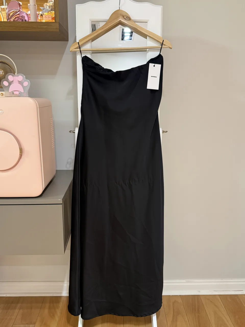 Vestido negro largo con tiras finas y escote recto. Posee una etiqueta blanca con el logo de la marca.