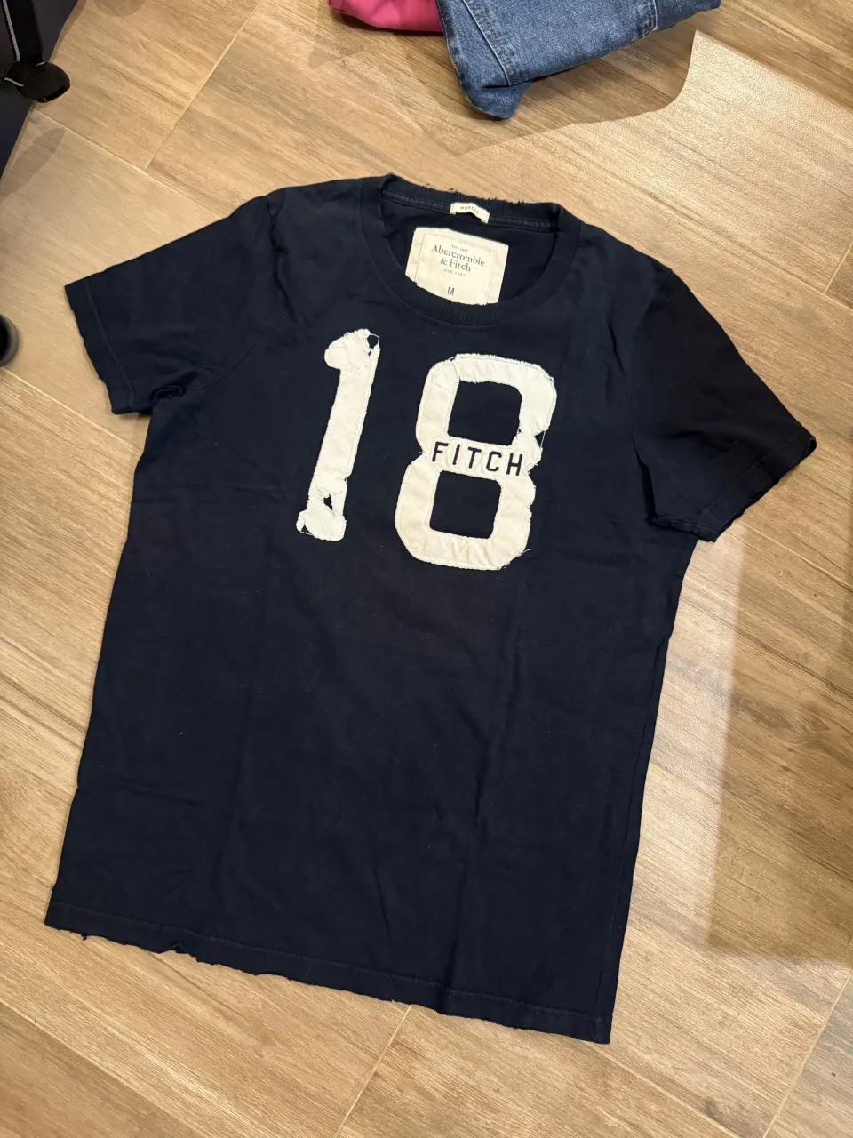 Remera azul marino con estampa de número 18 y la palabra "FITCH" en blanco. Cuello redondo y mangas cortas. Efecto roto