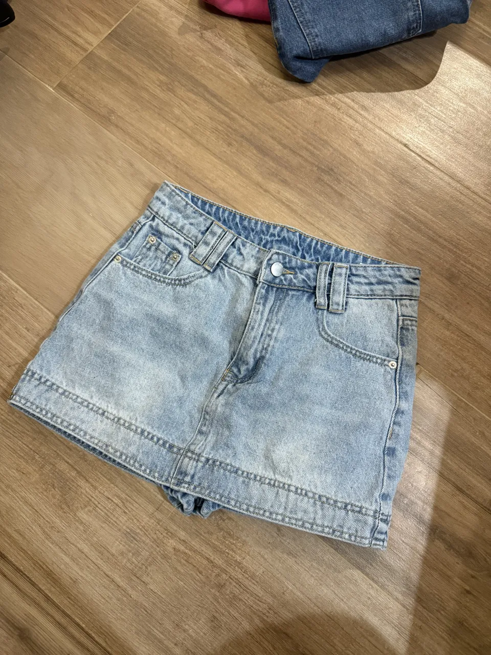 Pollera de jean tiro alto, color celeste. Posee bolsillos delanteros y traseros. Tiene short 