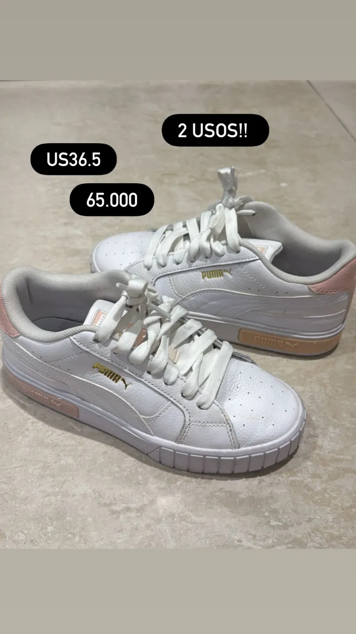 Zapatillas deportivas blancas con detalles en rosa pálido y suela blanca. Tienen cordones blancos y el logo de la marca en dorado.