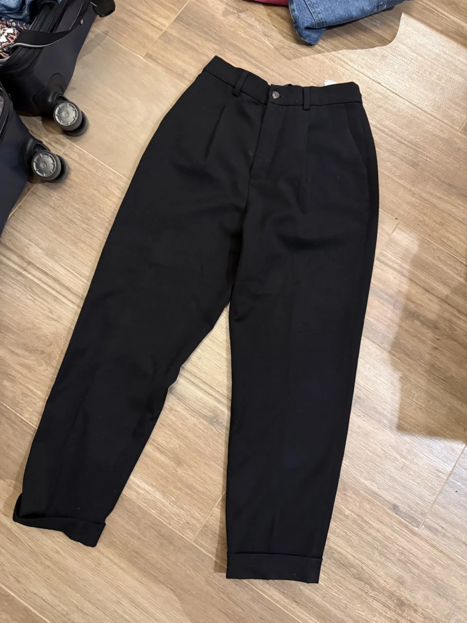 Pantalón negro de vestir con pinzas y puño en el ruedo. Contiene un par de pelotitas