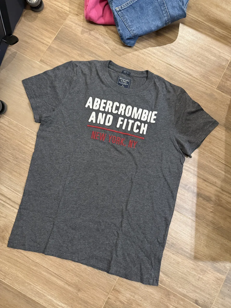 Remera gris de manga corta con estampa de la marca 'Abercrombie and Fitch' y 'New York, NY'.