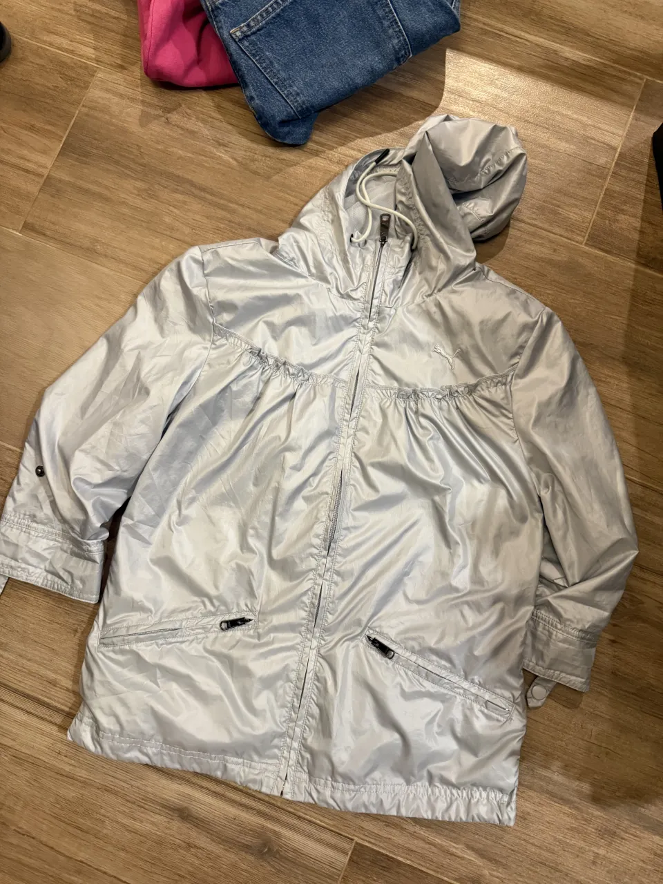 Campera plateada con capucha y cierre completo. Posee dos bolsillos frontales con cierre y detalles fruncidos en la parte superior del frente. Logo de la marca bordado en el pecho.
Impermeable. Dice L pero es un S/M