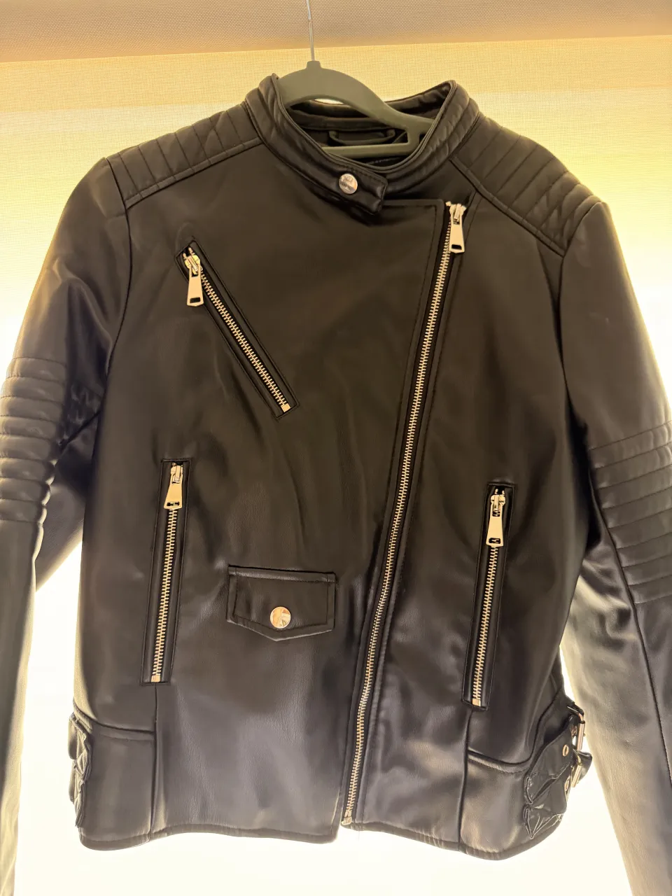 Campera de cuero sintético negra con cierre cruzado y múltiples bolsillos con cierre. Posee detalles acolchados en hombros y mangas.