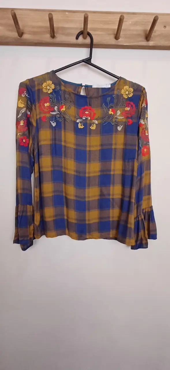 Blusa de mujer con estampado a cuadros en tonos amarillo y azul, con bordado floral en el cuello y mangas acampanadas. Ideal para un look casual y con estilo.