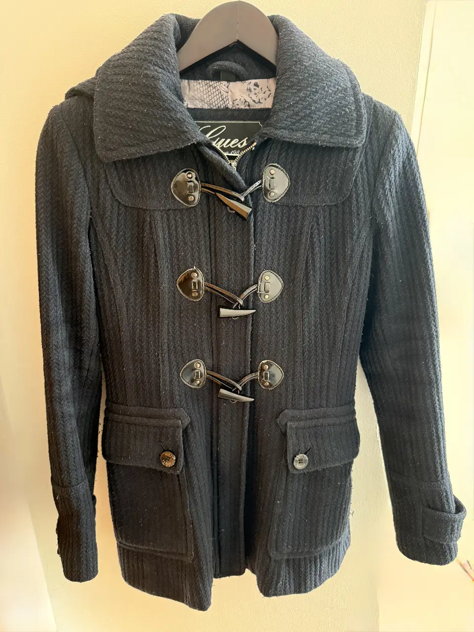 Tapado negro de paño con capucha y botones tipo duffle coat. Ideal para el invierno, este abrigo combina estilo y abrigo. Perfecto para un look casual y elegante.