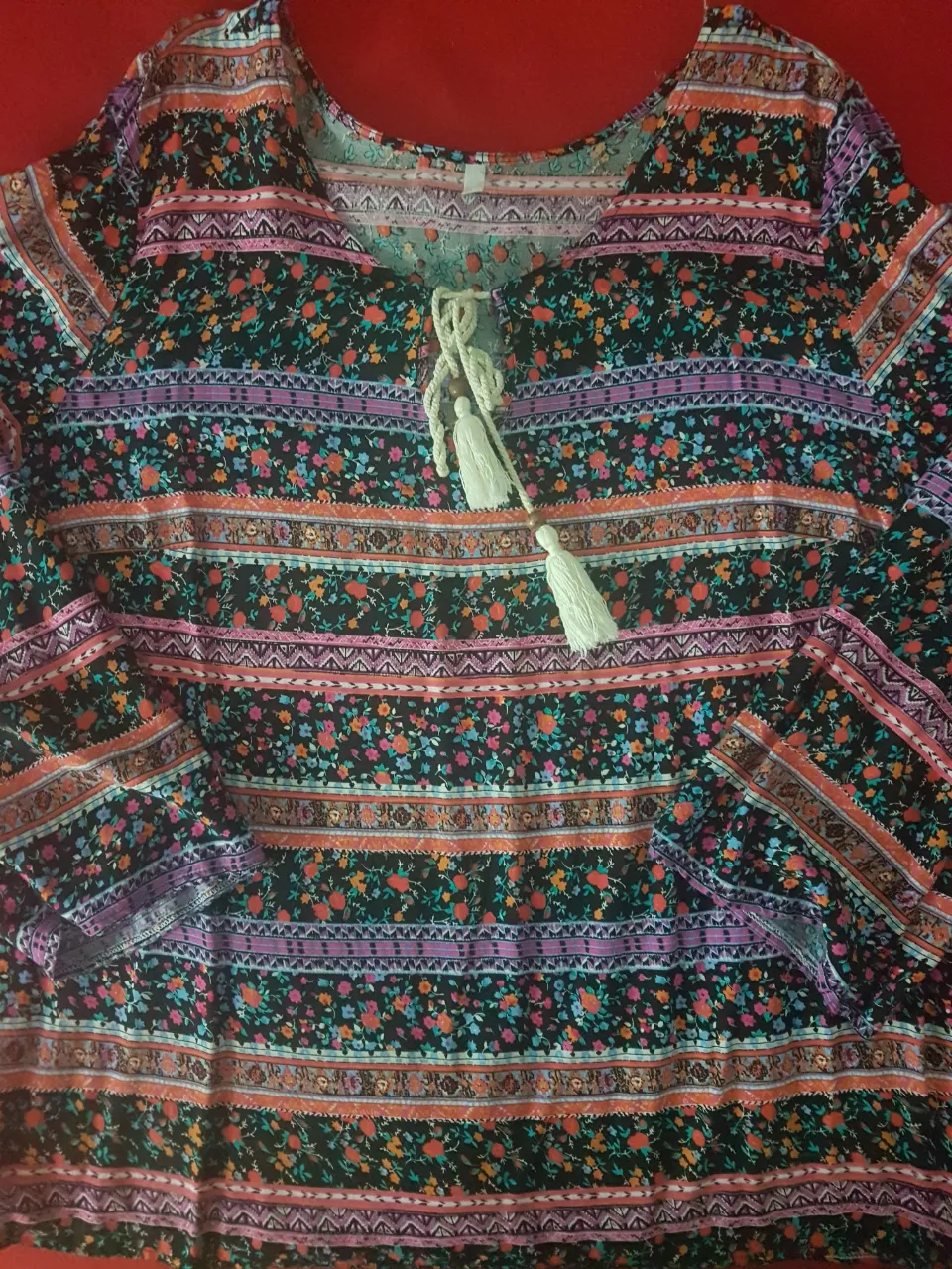 Remera manga larga estampada con flores y detalles étnicos. Posee cordones con pompones en el escote y un estilo bohemio.