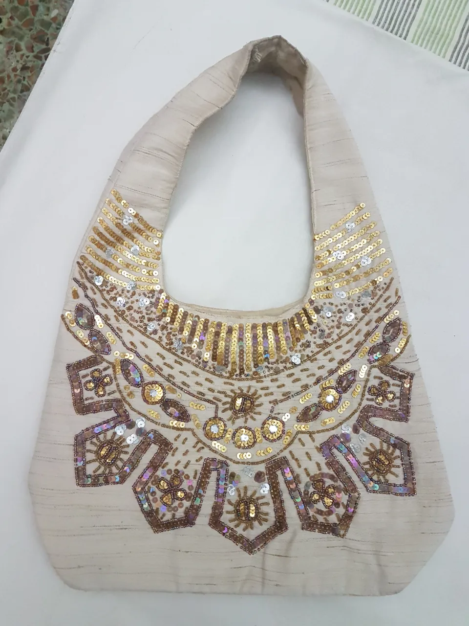 Bolso de mano beige con bordados y lentejuelas doradas y plateadas. Diseño único y llamativo, perfecto para darle un toque especial a tu outfit.