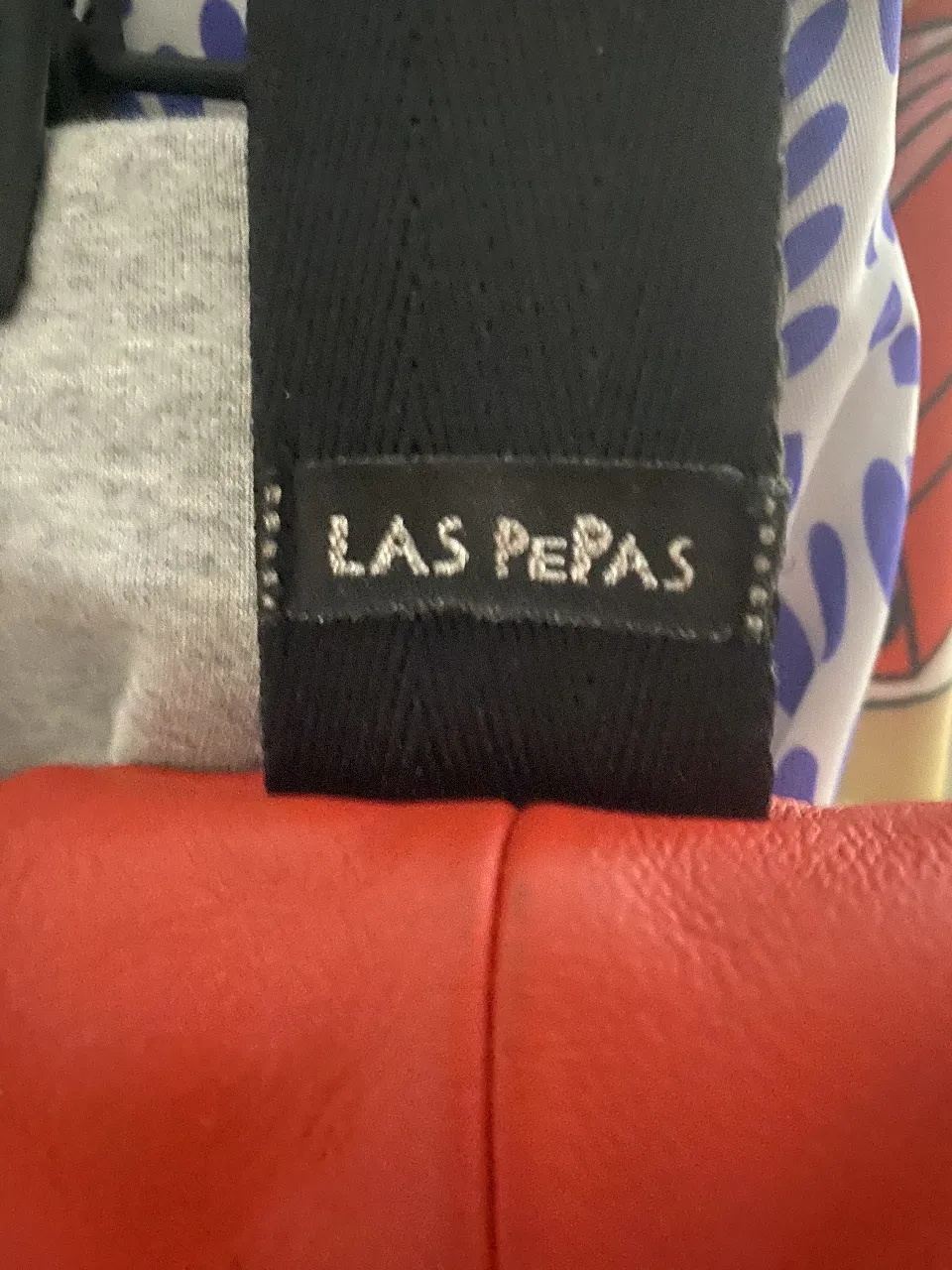 Cartera bandolera de cuero rojo, con etiqueta de la marca 'LAS PEPAS'. Ideal para llevar tus esenciales con estilo y comodidad.