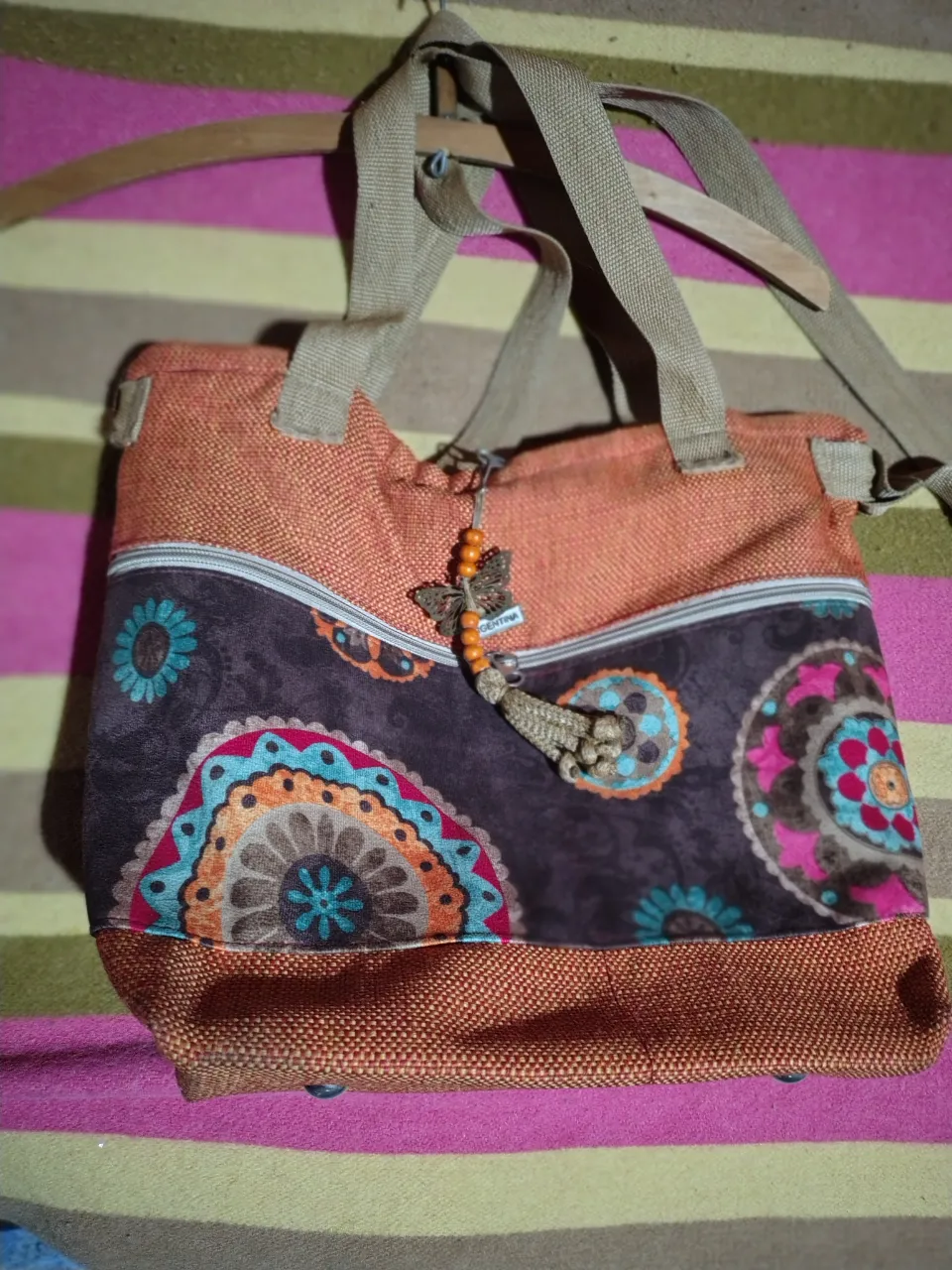 Cartera de hombro con diseño floral y detalles en naranja. Interior forrado en color violeta. Ideal para un look casual y con estilo.