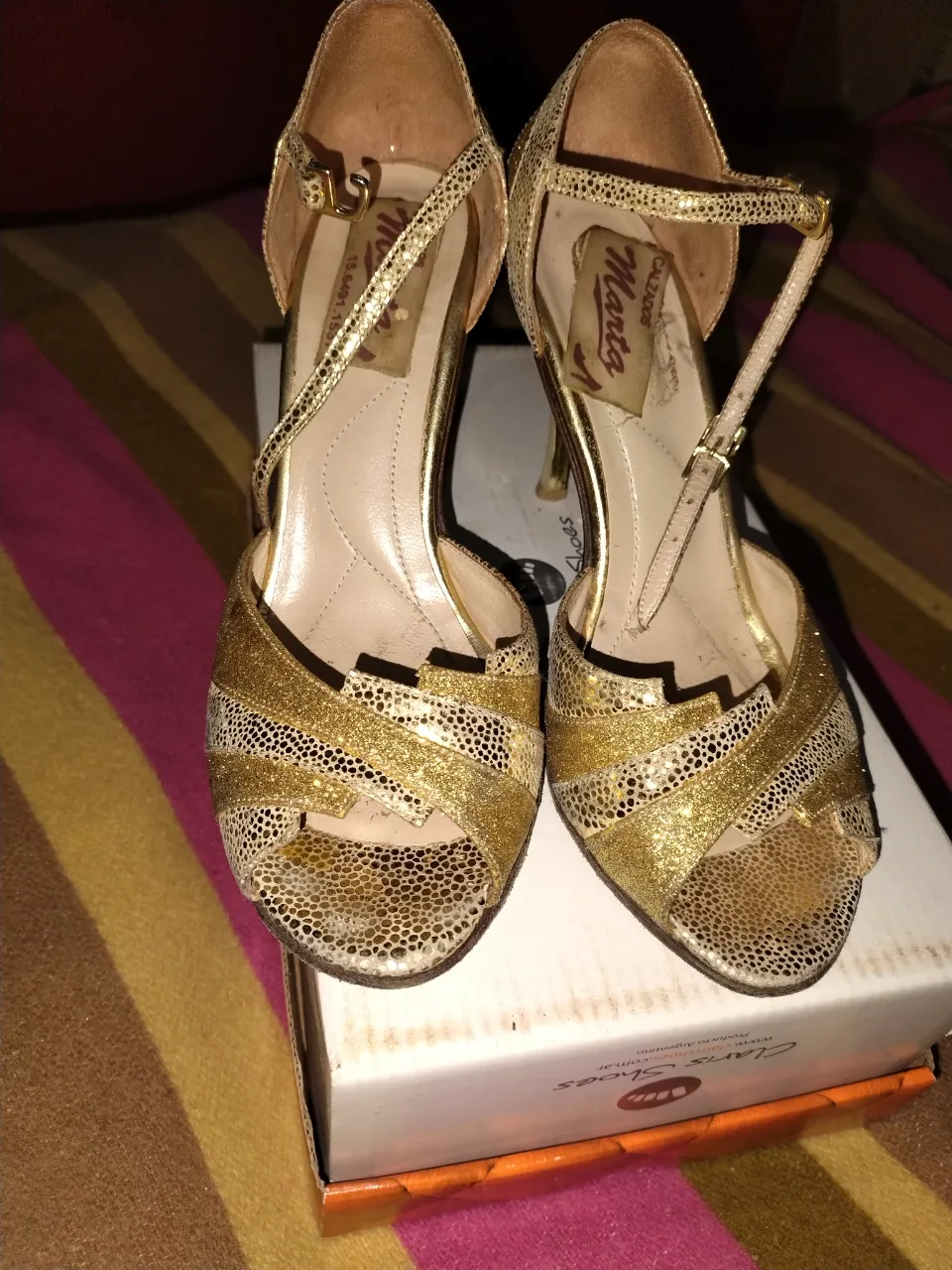 Sandalias de fiesta doradas con taco fino y pulsera al tobillo. Diseño elegante y sofisticado, ideales para eventos especiales.
