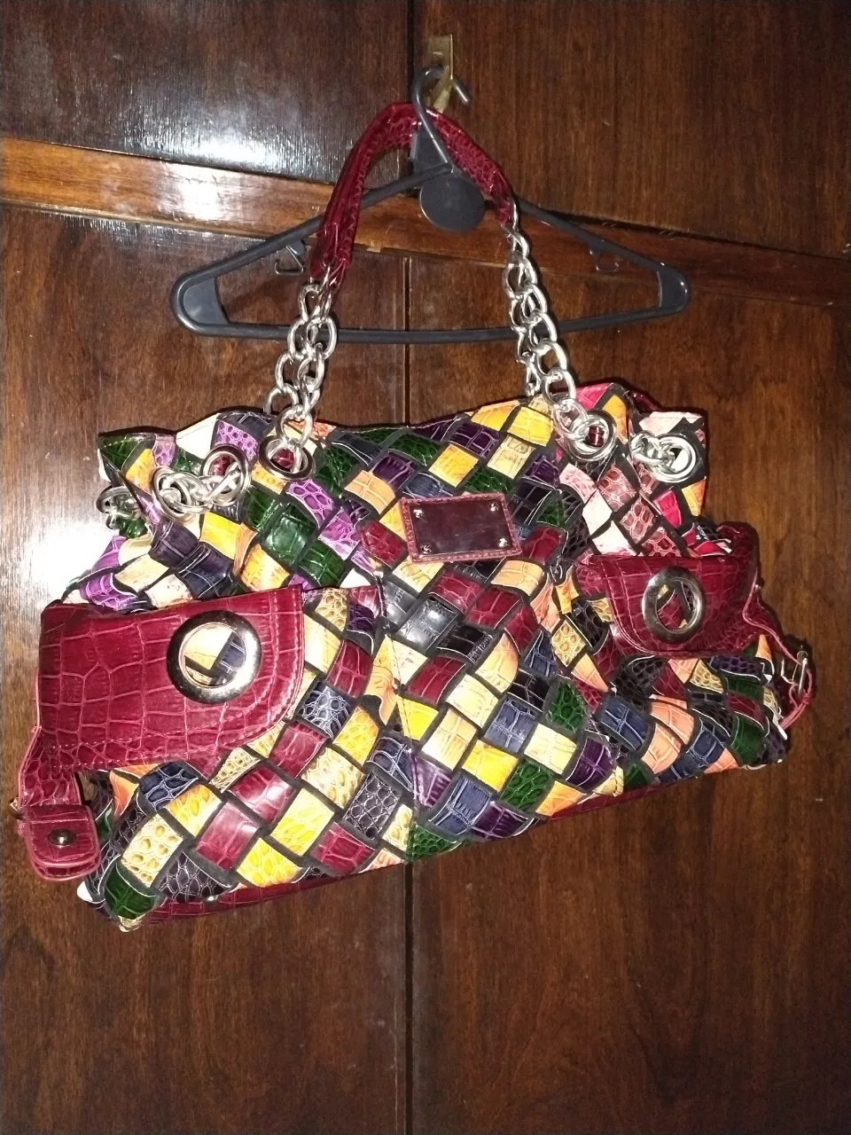 Cartera de mano multicolor con detalles en rojo y cadena plateada. Diseño tejido y detalles de cuero. Ideal para un look casual y con estilo.