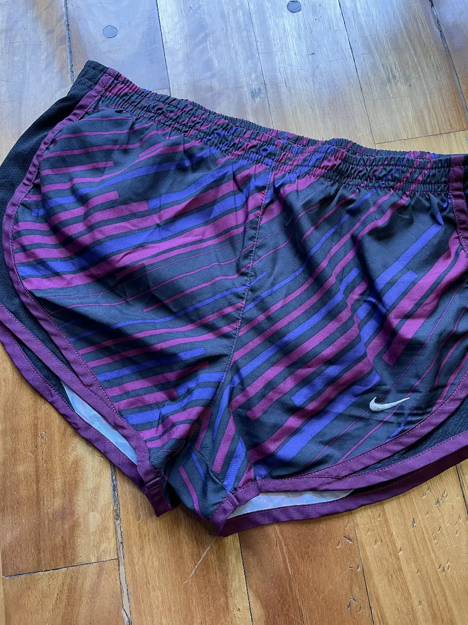 Short deportivo Nike para mujer, con estampado a rayas en tonos violeta y negro. Ideal para running y entrenamientos.