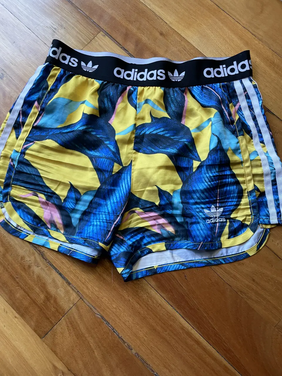 Short deportivo Adidas con estampado floral en tonos amarillos y azules. Cintura elastizada con logo de la marca. Ideal para actividades deportivas o uso casual.