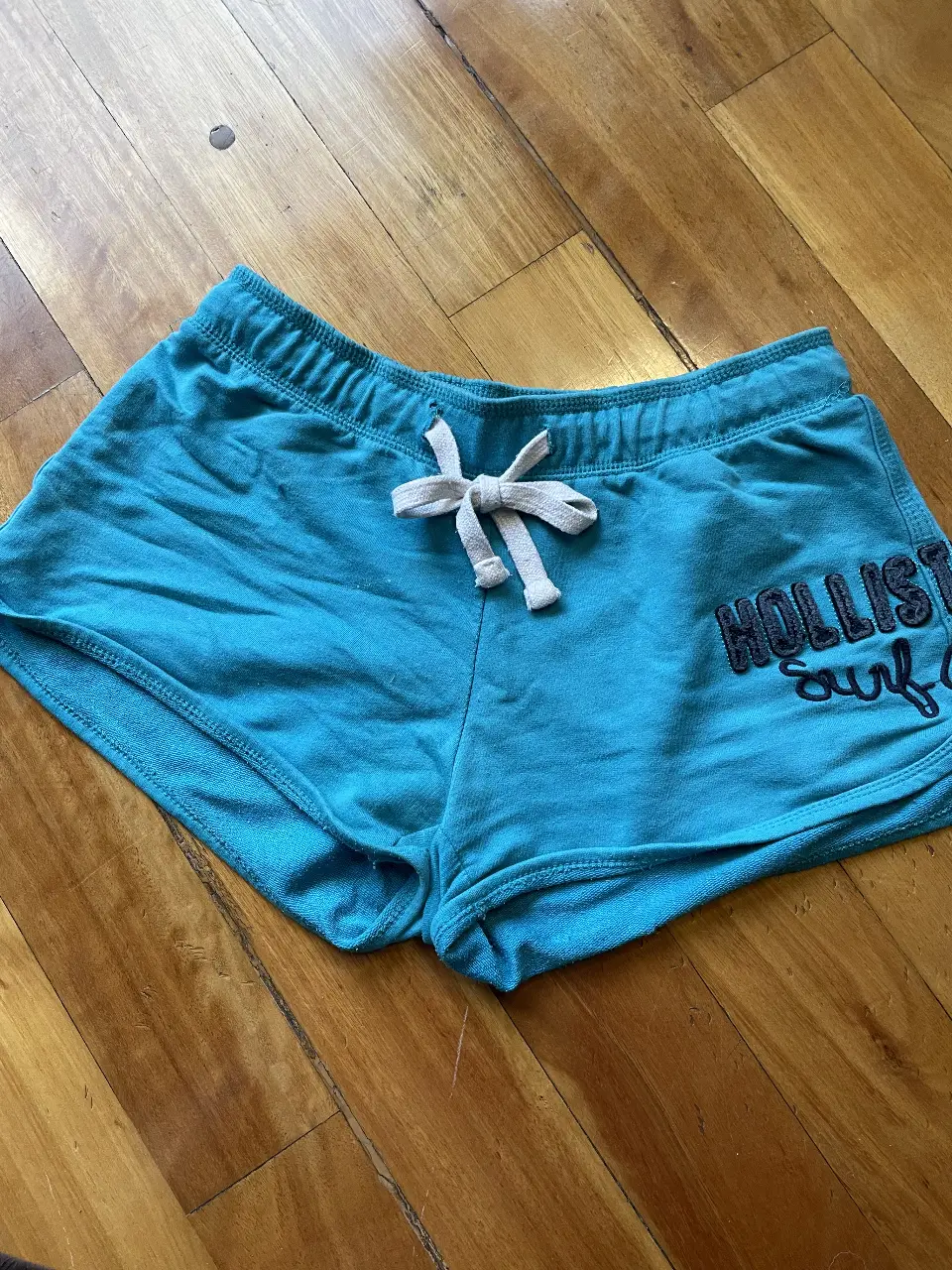 Short deportivo de mujer, color turquesa, con el logo de Hollister bordado. Ideal para actividades físicas o para un look casual y cómodo.