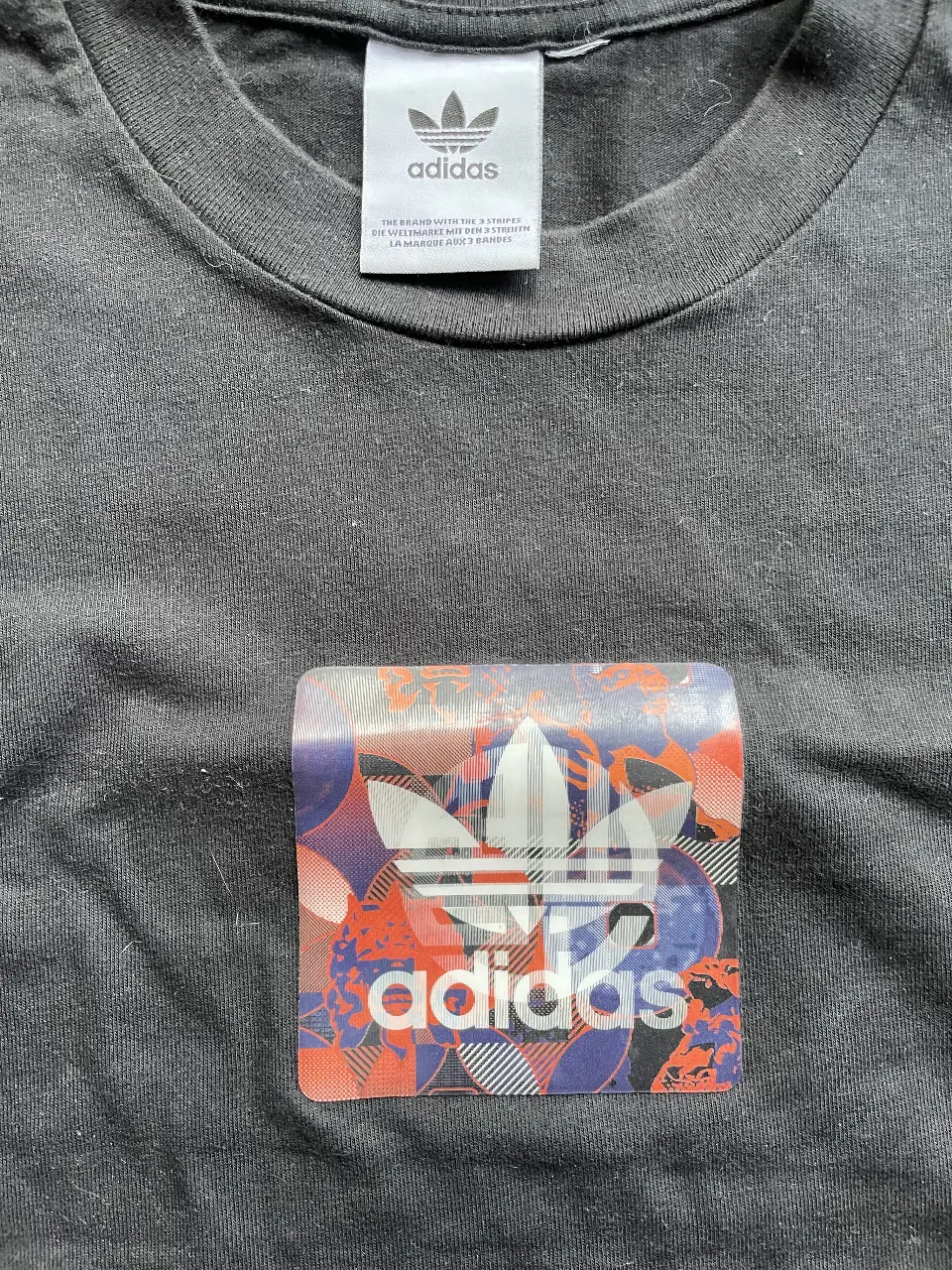Remera Adidas negra con estampado de logo multicolor en el frente. Ideal para un look casual y deportivo.