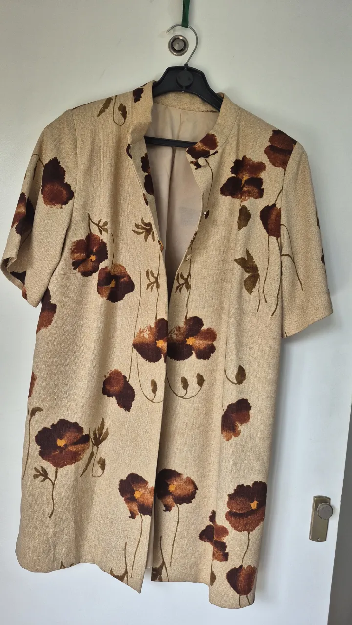 blazers  liviano con estampado floral de amapolas en tonos marrones y ocres sobre fondo beige. Posee cuello mao, manga corta y se abrocha al frente con tres botones. Tiene tajos laterales con botones y esta forrado