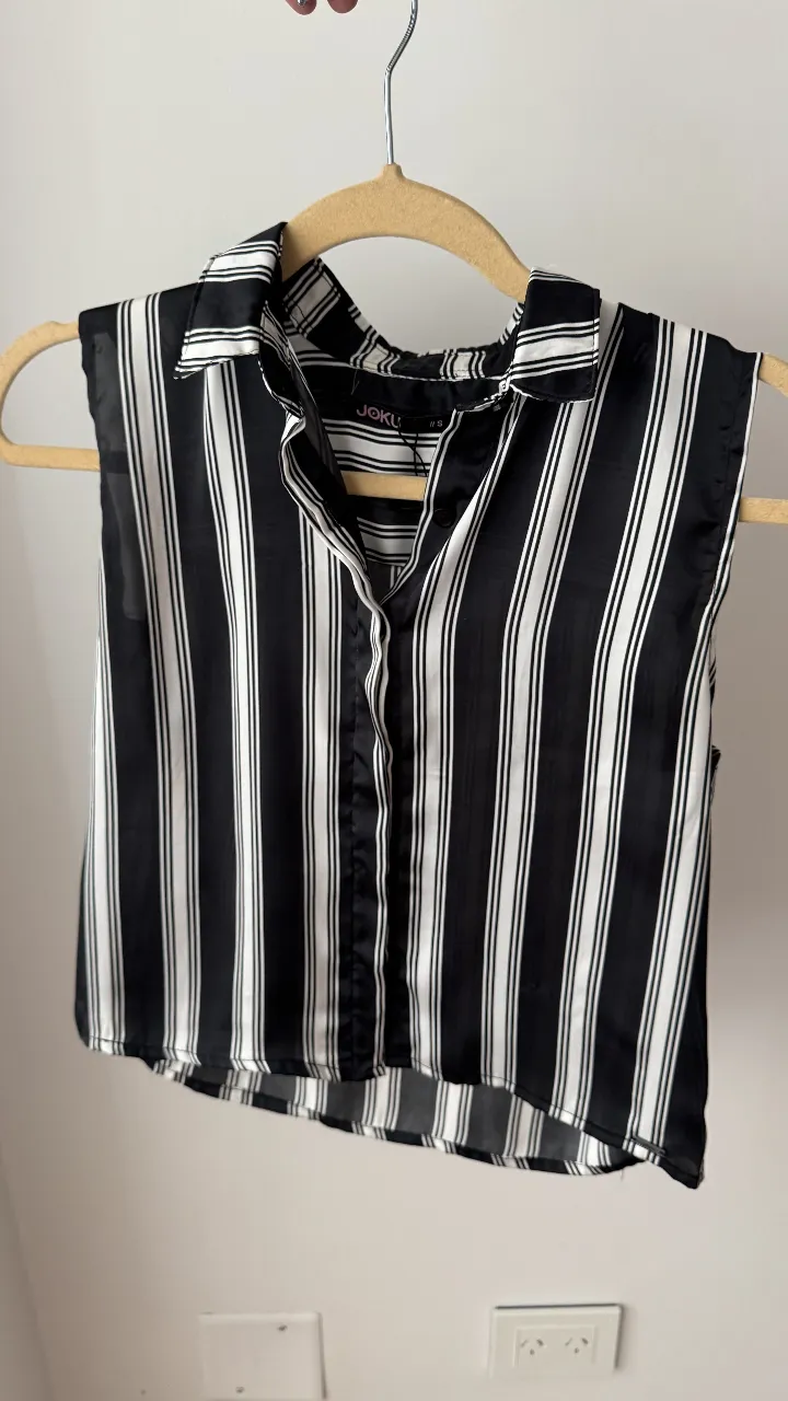 Camisa a rayas verticales blancas y negras, sin mangas y con cuello camisero. Ideal para un look canchero y moderno.