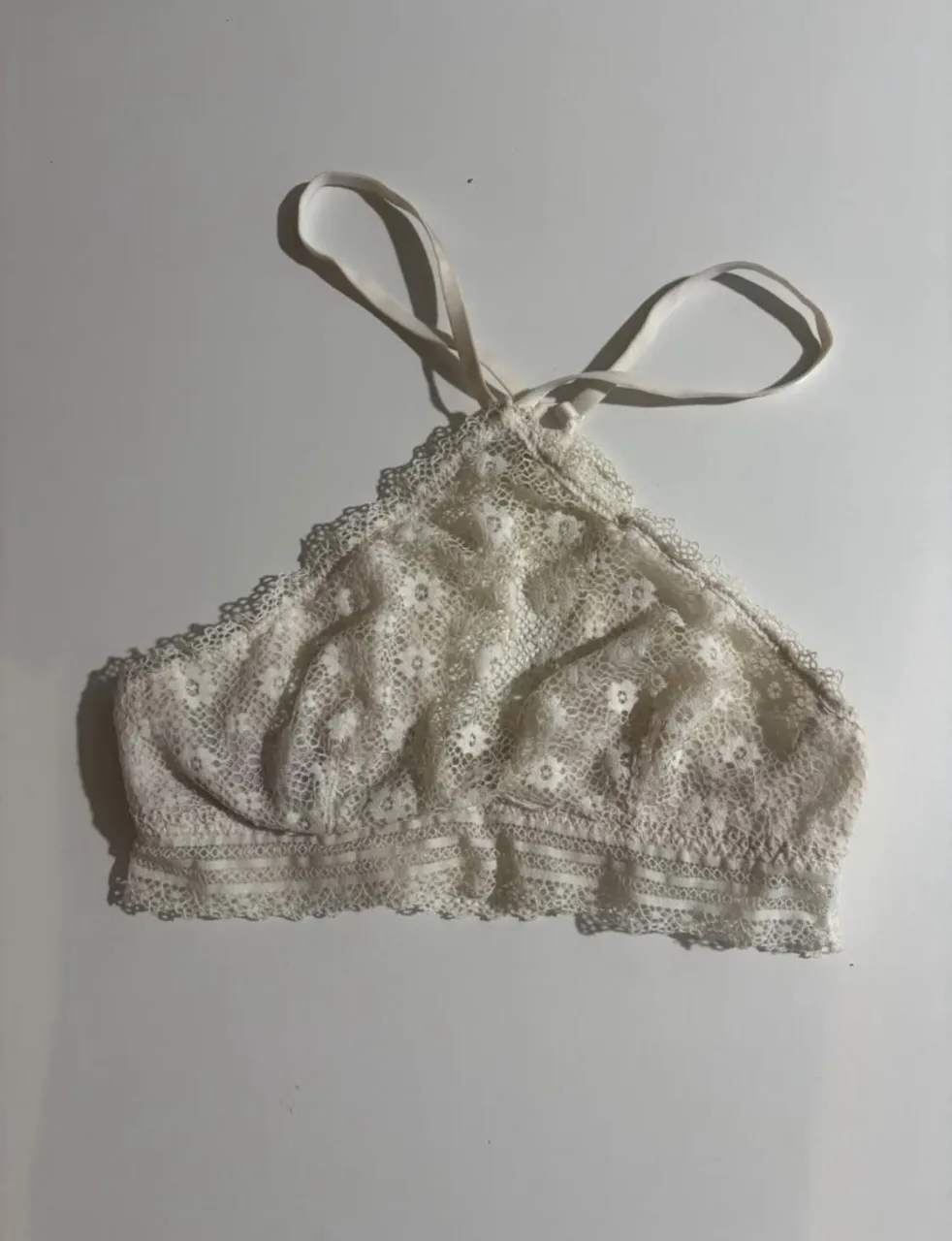 Corpiño de encaje blanco con detalles florales y borde de puntilla. Breteles finos regulables.