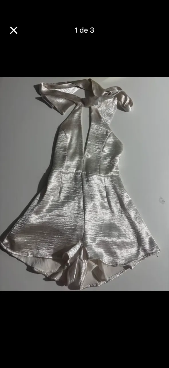 Mono corto blanco con escote halter y lazo en la espalda. Posee detalles texturizados en la tela y un corte acampanado en la parte inferior.