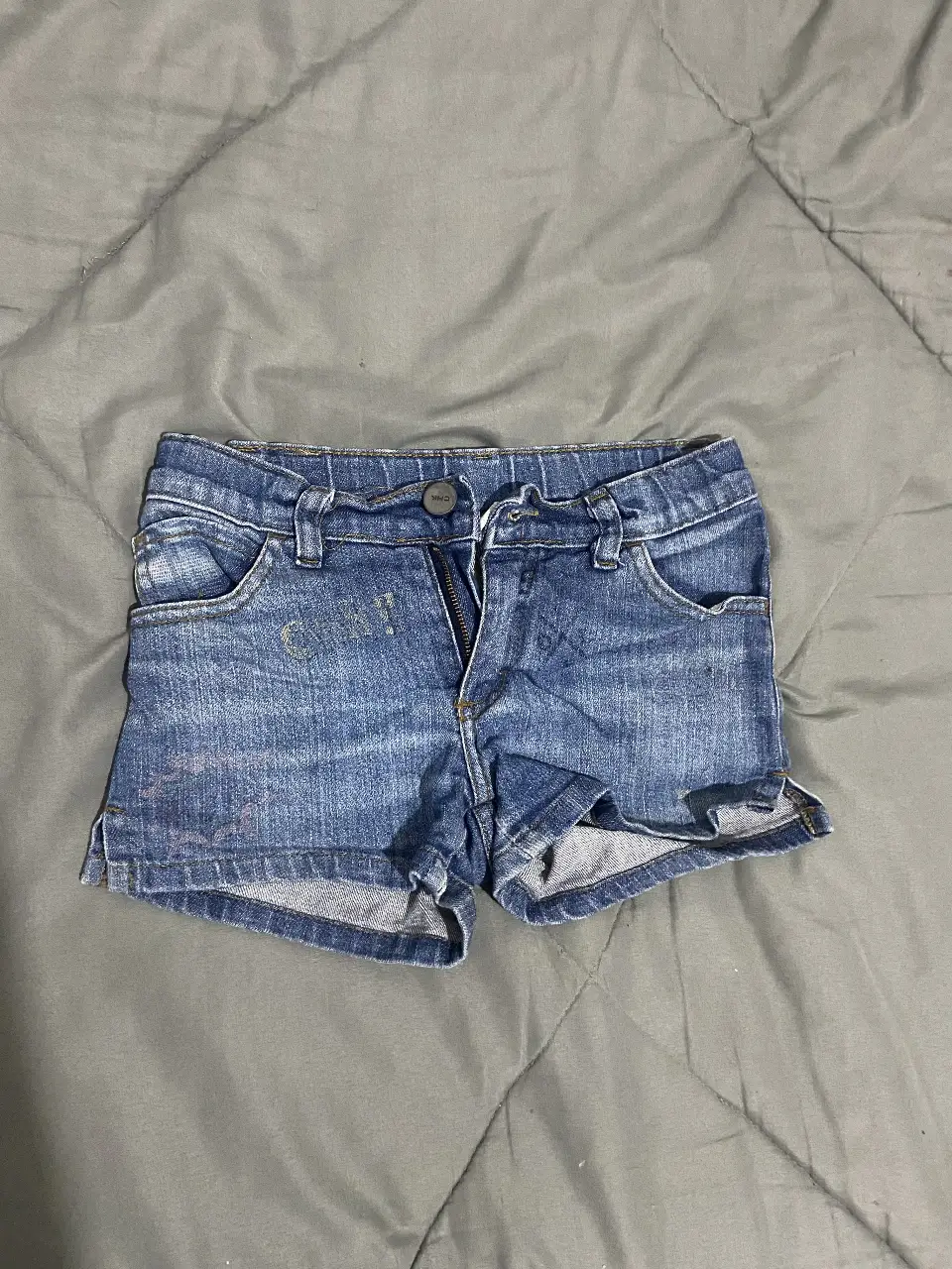 Short de jean azul para niña, con detalles de desgaste y etiqueta CHK. Ideal para un look casual y cómodo.