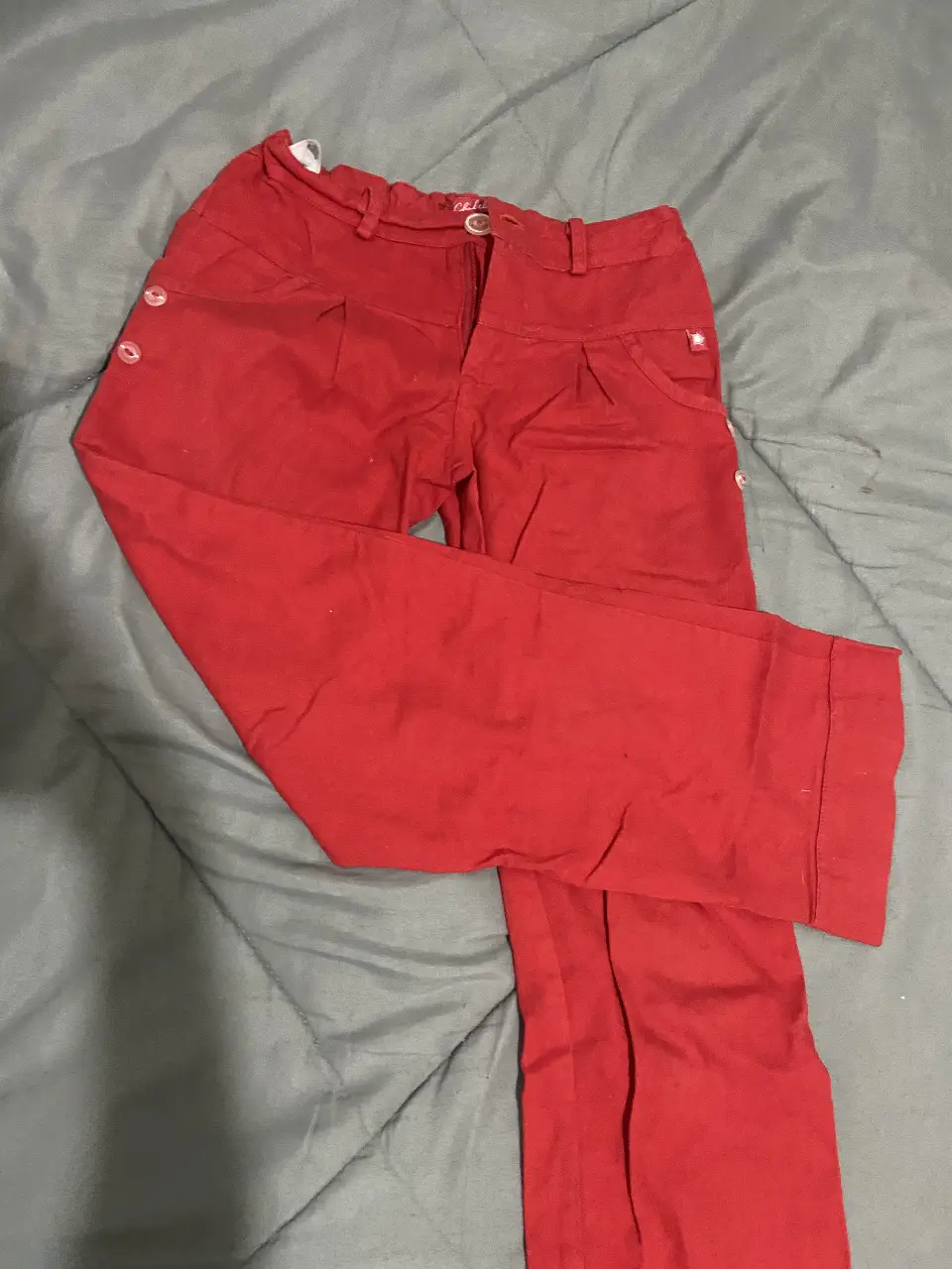 Pantalón rojo de niña, con detalles de botones en los laterales y cierre. Ideal para un look casual y cómodo.