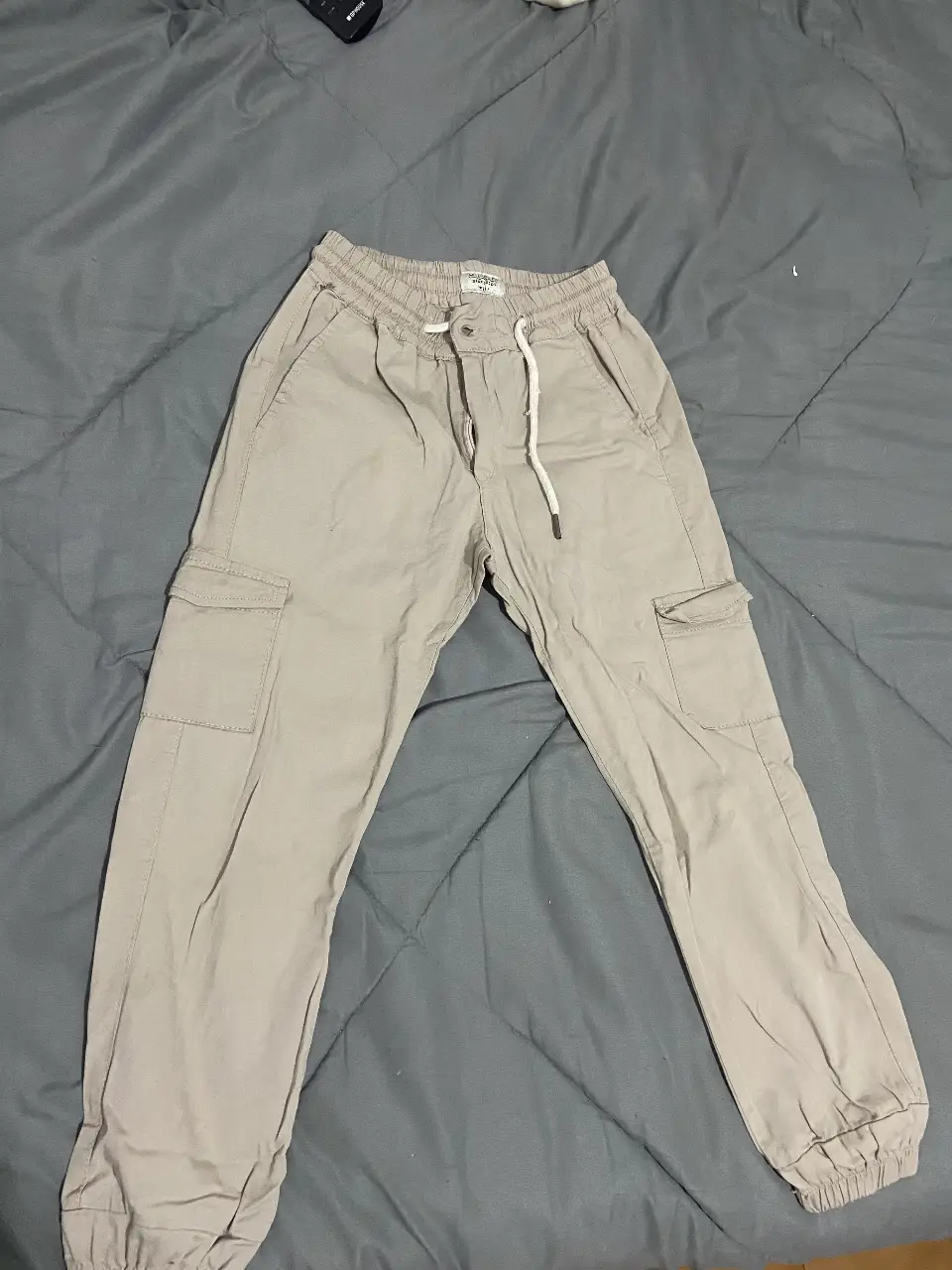 Pantalón cargo de hombre en color gris claro. Confeccionado en tela resistente, presenta múltiples bolsillos y cintura elastizada con cordón. Ideal para un look casual y funcional.