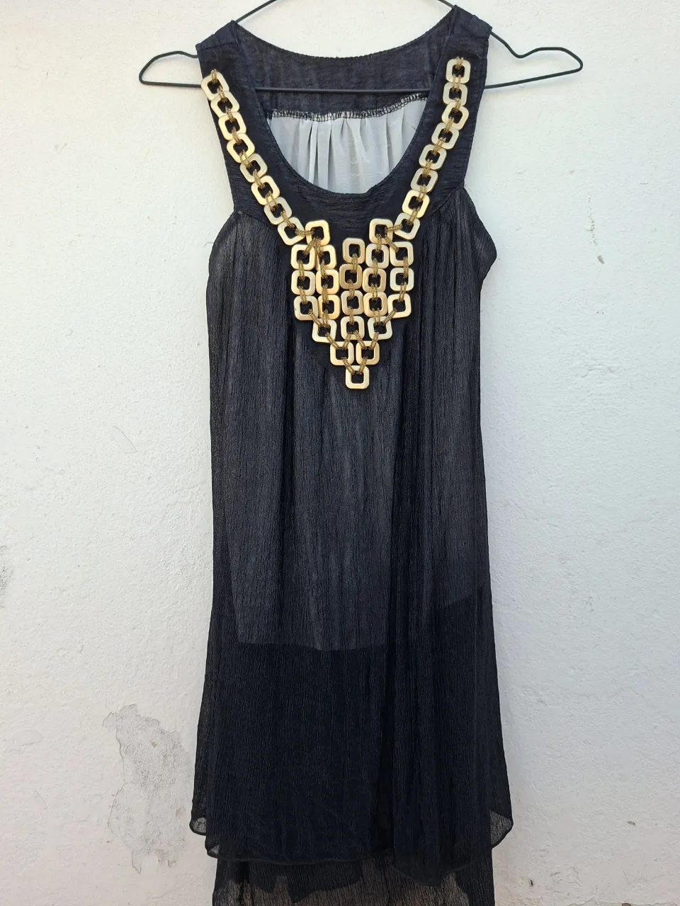 Vestido negro con un espectacular detalle de cadena dorada en el escote, que le da un toque de glamour y sofisticación. Ideal para lucir en una salida nocturna o una fiesta.