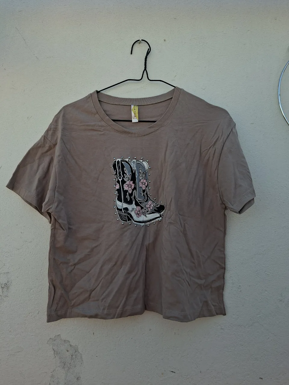 Remera crop color tiza con estampa de botas tejana estilo western con detalles de flores y tachas. Un diseño único y canchero para lucir tu estilo.