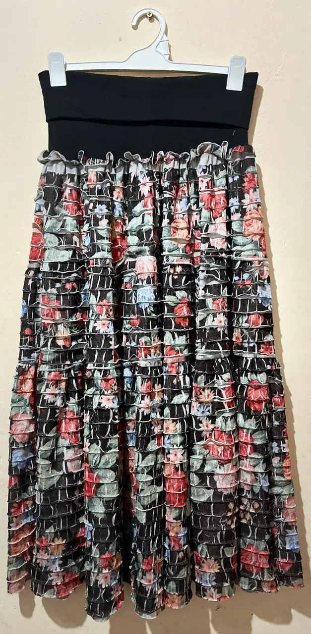 Pollera larga con estampado floral en tonos rojos, rosas y azules sobre fondo negro. Diseño con volados y cintura ancha elástica.