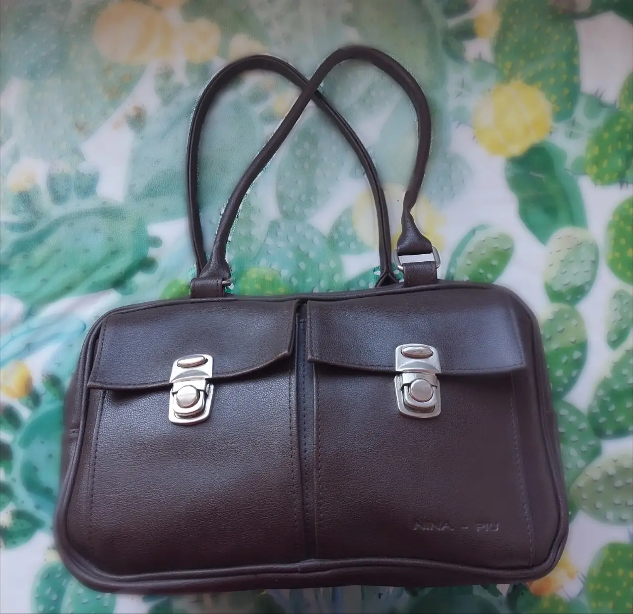 Cartera de mano marrón de cuero, con dos compartimentos frontales con cierre de broche plateado. Ideal para un look elegante y funcional.