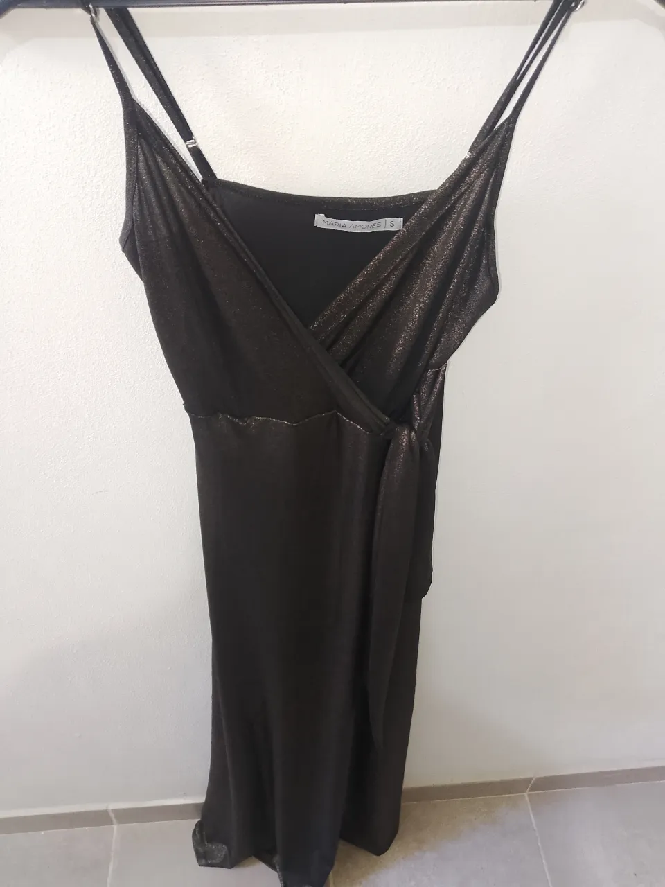 Vestido largo negro con brillos, ideal para fiestas o eventos especiales. Posee breteles finos y un lazo para atar en la cintura, que le da un toque elegante y femenino. Su diseño cruzado en la parte superior lo hace súper favorecedor.
