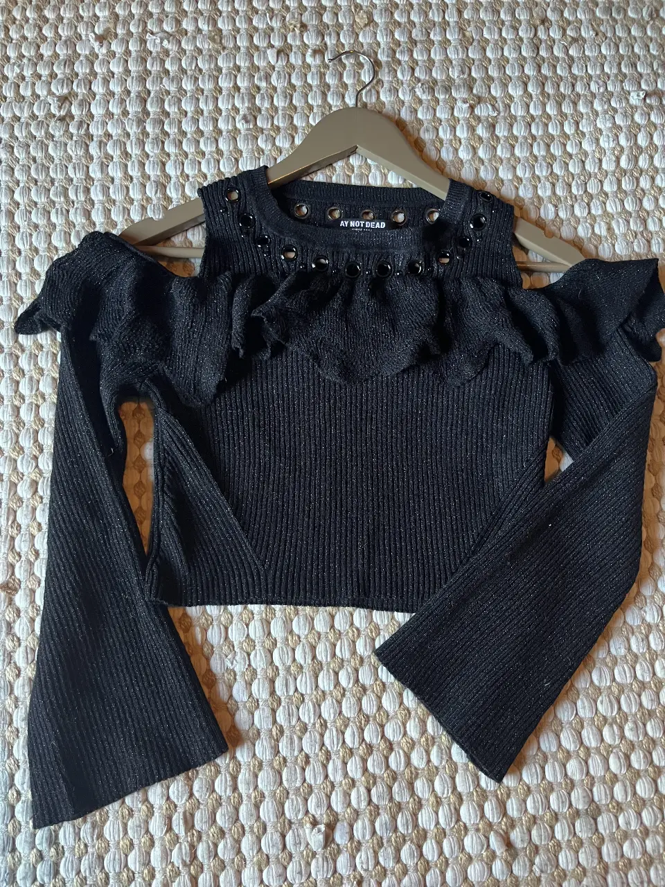 Sweater negro con detalles de arandelas y volados en el cuello. Ideal para un look rocker y moderno.