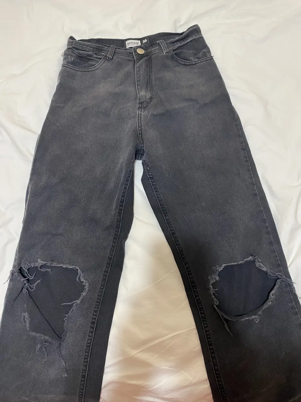 Jeans negro gastado con roturas en las rodillas, tiro alto, ideal para un look casual y moderno.