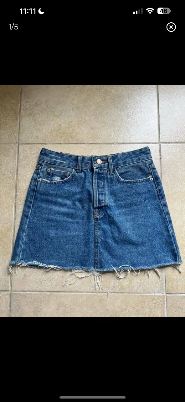 Minifalda de jean azul, con un corte recto y un dobladillo deshilachado que le da un toque moderno y casual. Ideal para un look urbano y relajado.