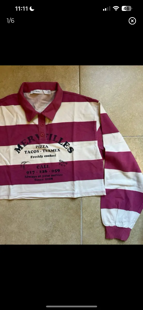 Remera manga larga crop con cuello polo a rayas rosas y blancas. Estampado frontal con diseño de "Merveilles Pizza Tacos Texmex". Ideal para un look casual y retro.